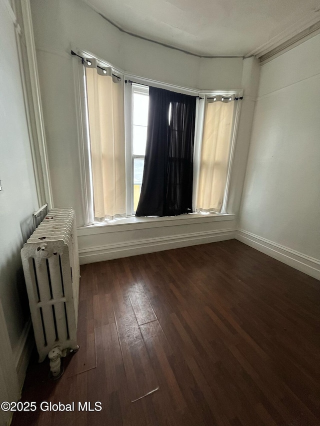 unfurnished room featuring hardwood / wood-style floors, radiator, and baseboards