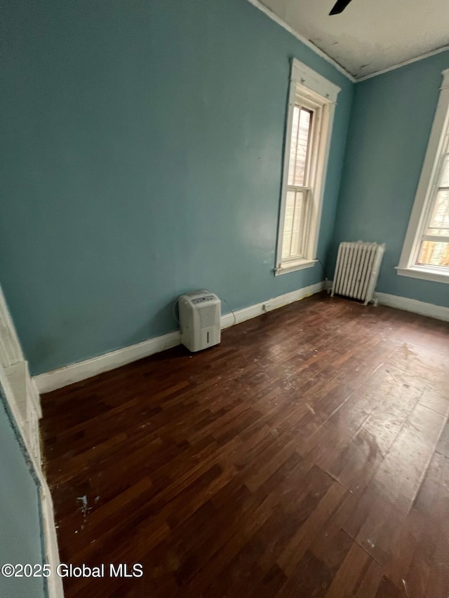 unfurnished room featuring baseboards, ceiling fan, radiator heating unit, ornamental molding, and dark wood-style flooring