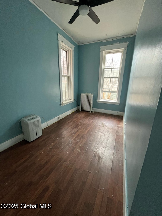 empty room with radiator, dark wood-style flooring, a wealth of natural light, and ornamental molding