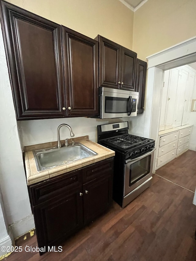 kitchen with dark wood-style flooring, a sink, tile counters, dark brown cabinetry, and appliances with stainless steel finishes