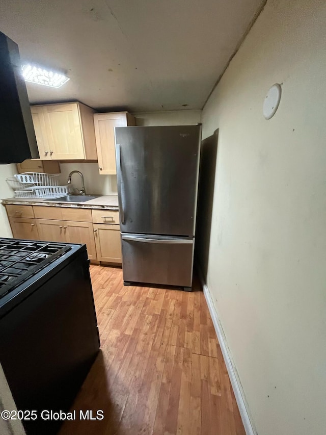 kitchen featuring baseboards, light wood-type flooring, freestanding refrigerator, black range with gas cooktop, and a sink