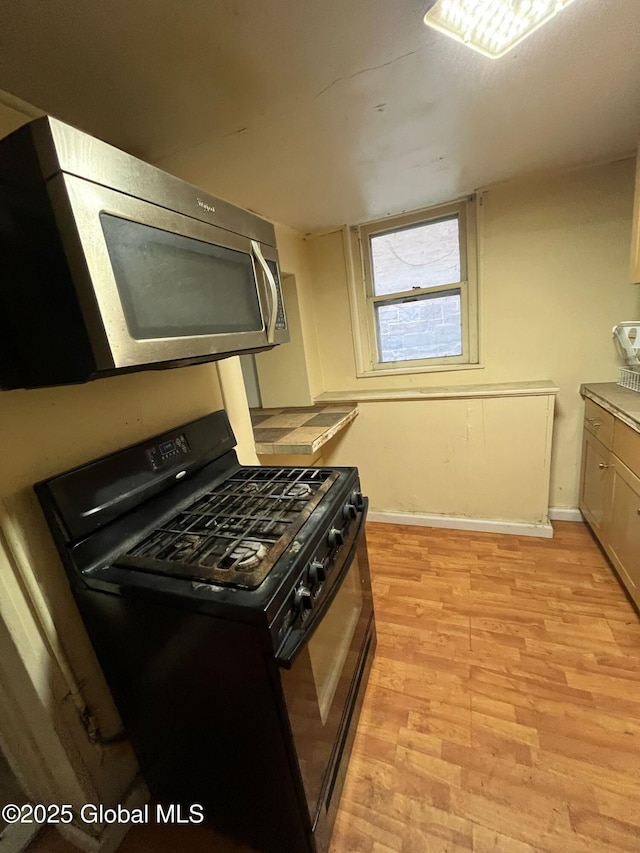 kitchen featuring light wood-type flooring, stainless steel microwave, baseboards, and black range with gas stovetop