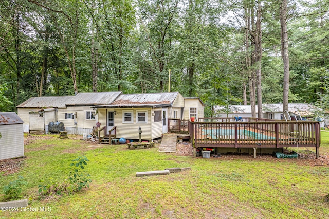 rear view of property featuring a yard, entry steps, an outdoor structure, a deck, and metal roof