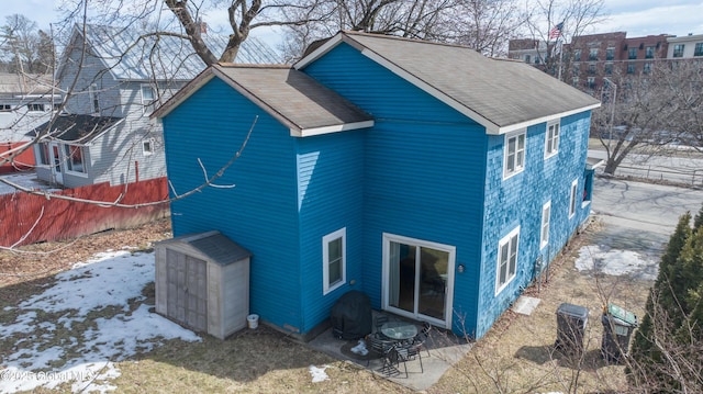 snow covered house featuring fence and roof with shingles