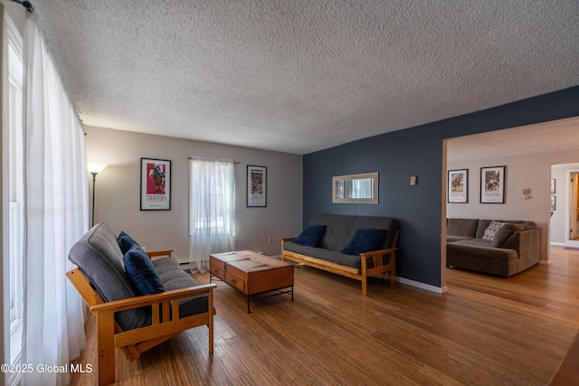 living area with a textured ceiling, a baseboard heating unit, baseboards, and wood finished floors