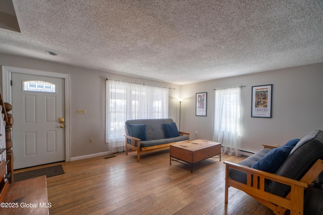 living area featuring a healthy amount of sunlight, a textured ceiling, baseboards, and wood finished floors