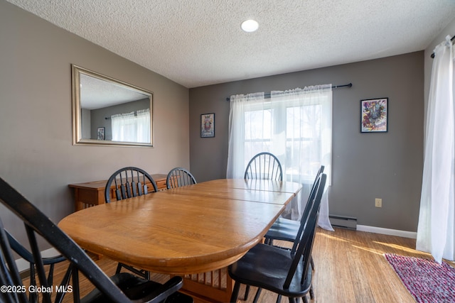 dining room featuring a baseboard radiator, baseboards, a textured ceiling, and light wood finished floors