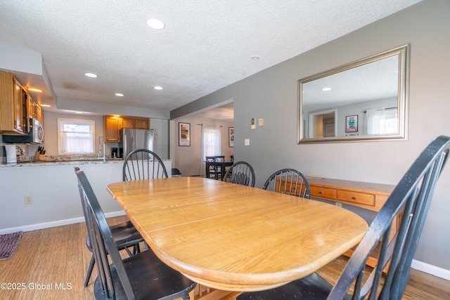 dining space with recessed lighting, light wood-style flooring, a textured ceiling, and baseboards