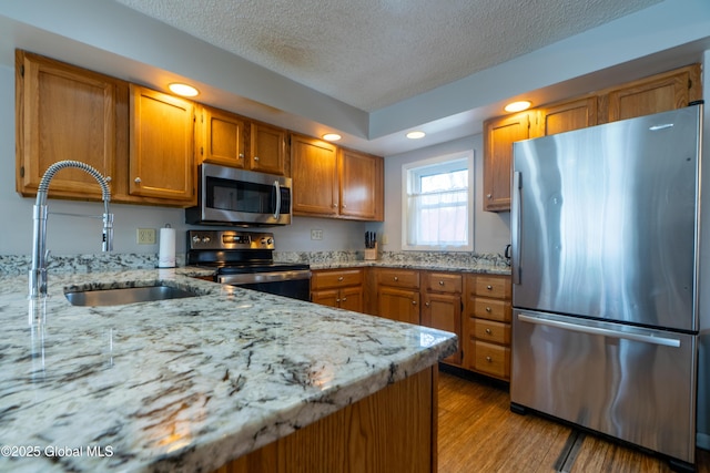 kitchen with light stone counters, light wood-style flooring, a sink, stainless steel appliances, and brown cabinets