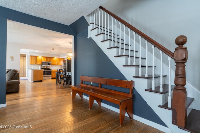 stairway featuring baseboards, a textured ceiling, and wood finished floors