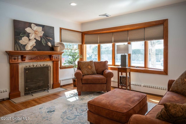 living area with visible vents, a healthy amount of sunlight, a baseboard heating unit, and wood finished floors