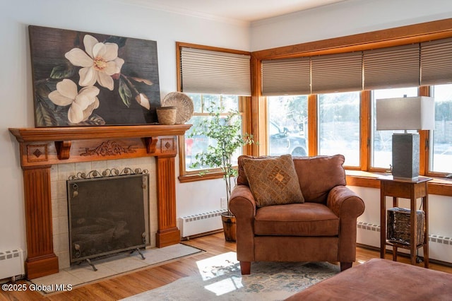 living area with a baseboard radiator, wood finished floors, crown molding, and a tile fireplace