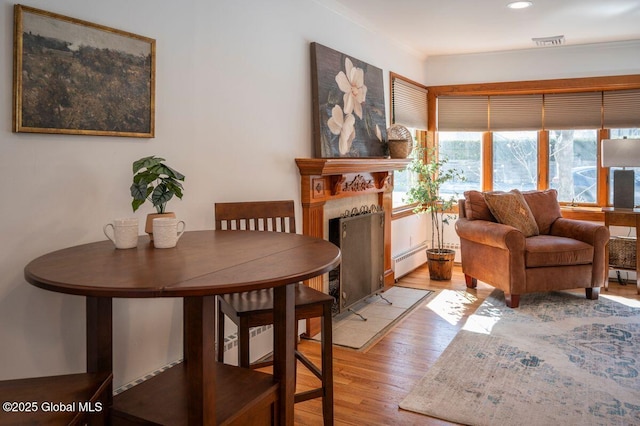 dining room with a baseboard radiator, a fireplace with flush hearth, visible vents, and light wood finished floors