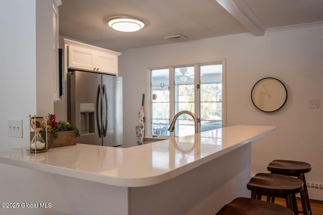 kitchen with a breakfast bar area, visible vents, beam ceiling, white cabinets, and stainless steel refrigerator with ice dispenser