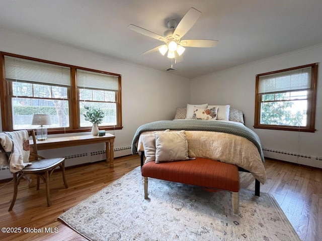 bedroom featuring multiple windows, wood finished floors, ornamental molding, and a baseboard radiator