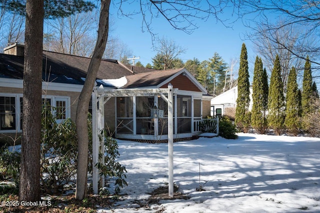 snow covered back of property featuring brick siding, a chimney, and a sunroom