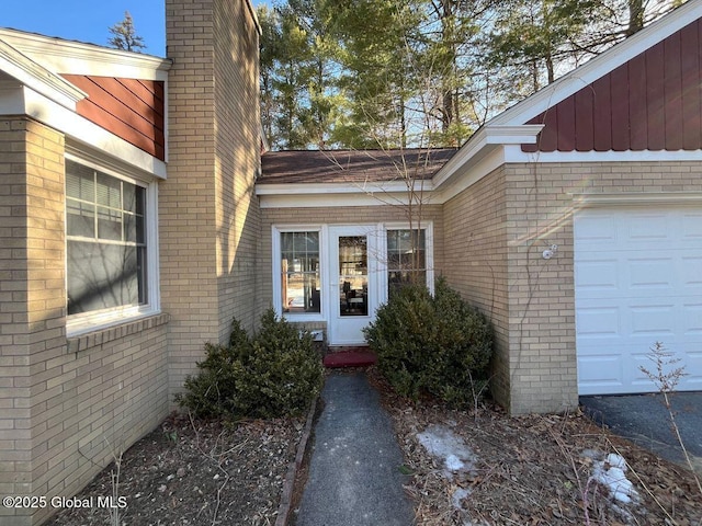 entrance to property with brick siding, a chimney, and a garage