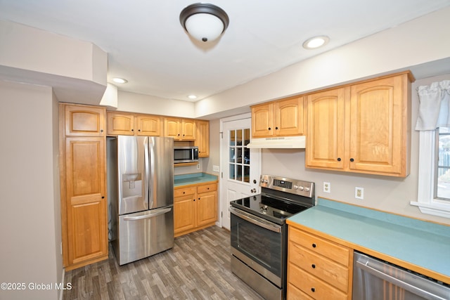 kitchen featuring wood finished floors, light brown cabinets, stainless steel appliances, light countertops, and under cabinet range hood