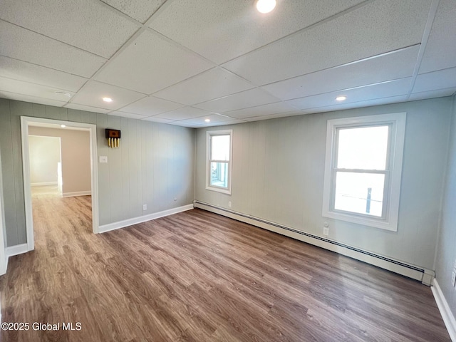 empty room with a baseboard radiator, a paneled ceiling, baseboards, and wood finished floors