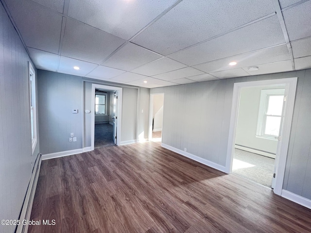 empty room with a drop ceiling, a baseboard heating unit, dark wood finished floors, and a baseboard radiator