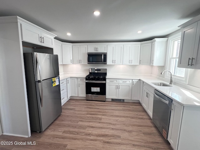 kitchen with white cabinets, appliances with stainless steel finishes, light wood-style floors, and a sink