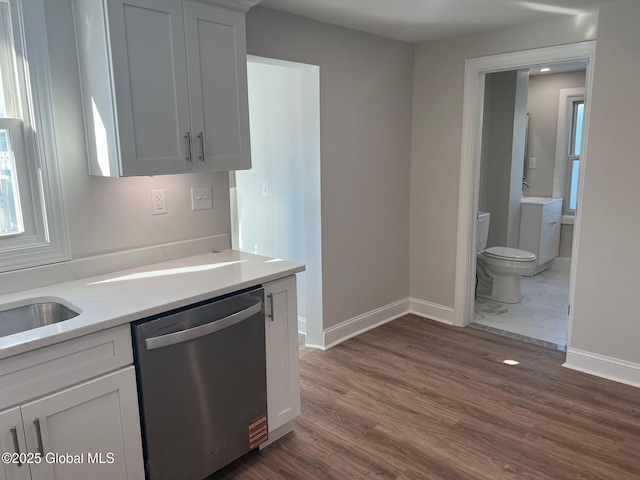 kitchen featuring stainless steel dishwasher, dark wood finished floors, baseboards, and white cabinetry