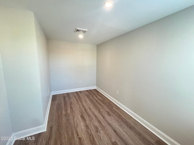 spare room featuring dark wood-type flooring, visible vents, and baseboards