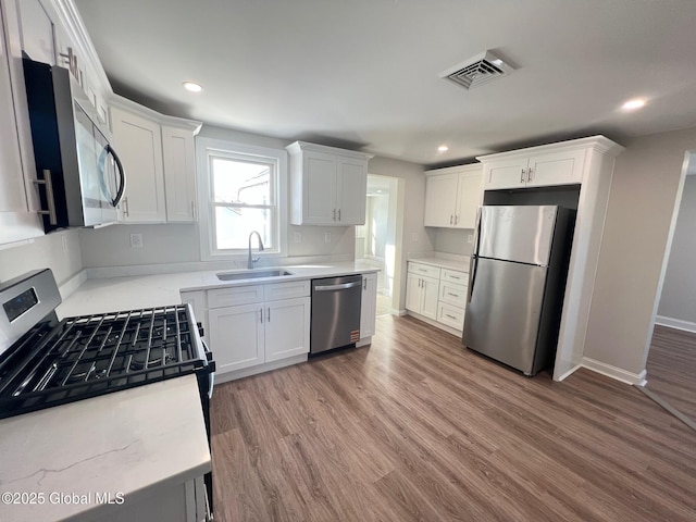 kitchen featuring visible vents, a sink, wood finished floors, appliances with stainless steel finishes, and white cabinets