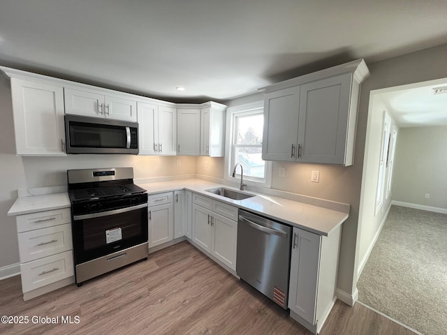 kitchen featuring baseboards, a sink, stainless steel appliances, light countertops, and white cabinetry