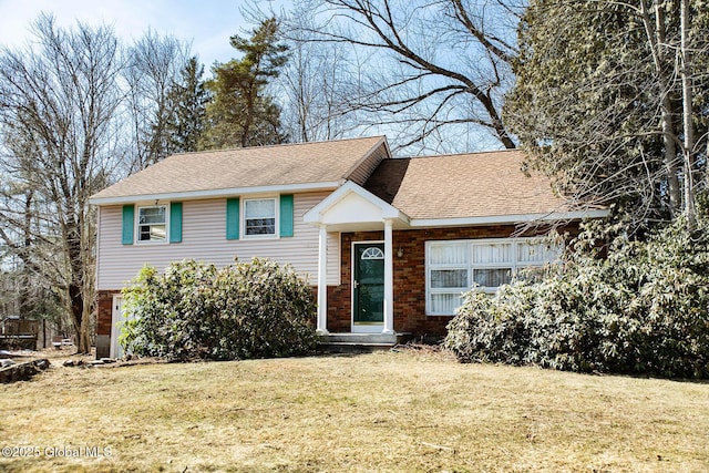 split level home featuring brick siding, roof with shingles, and a front lawn