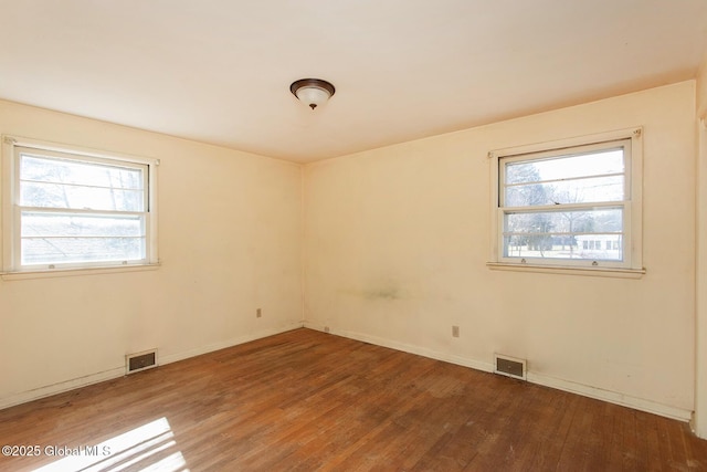 spare room featuring a wealth of natural light, visible vents, and wood finished floors