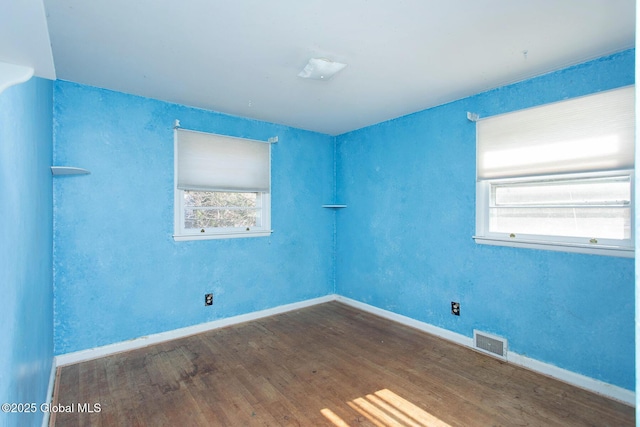 empty room with wood finished floors, visible vents, and baseboards