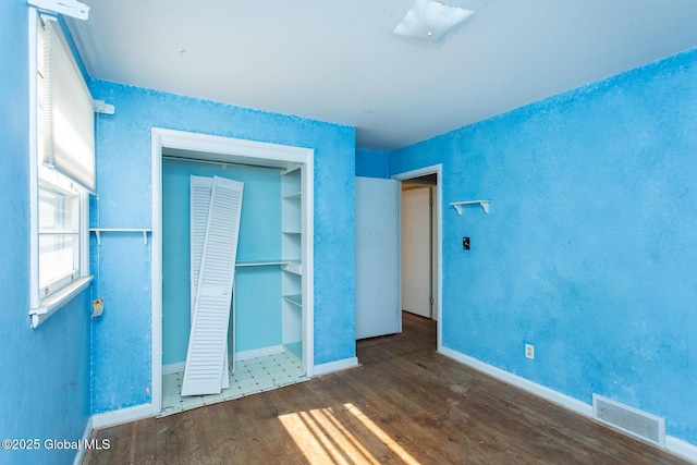 unfurnished bedroom with wood finished floors, visible vents, a closet, and baseboards