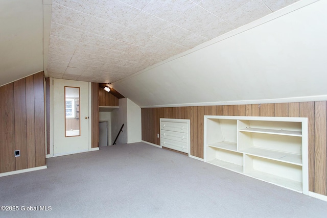 additional living space featuring built in shelves, lofted ceiling, wood walls, and carpet flooring