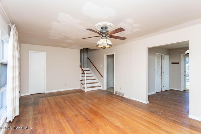 unfurnished room with ceiling fan, visible vents, wood finished floors, and stairs