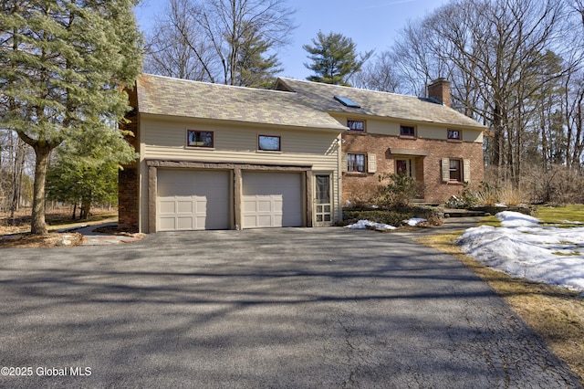 view of front of home featuring an attached garage, brick siding, driveway, and a chimney