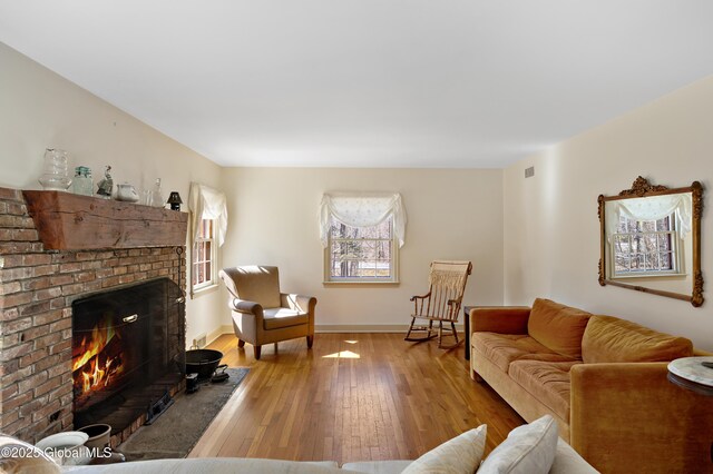 living room featuring visible vents, baseboards, a brick fireplace, and hardwood / wood-style floors