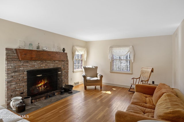 living room with visible vents, a fireplace, baseboards, and wood-type flooring