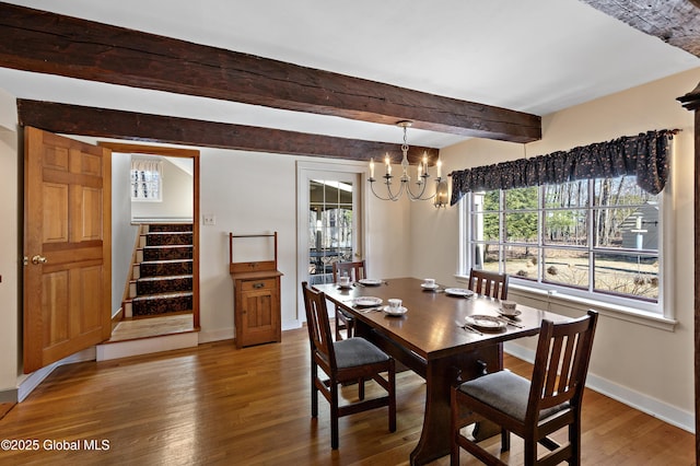 dining room with beam ceiling, wood finished floors, an inviting chandelier, baseboards, and stairs