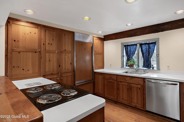 kitchen featuring stovetop with downdraft, brown cabinets, stainless steel dishwasher, paneled refrigerator, and a sink