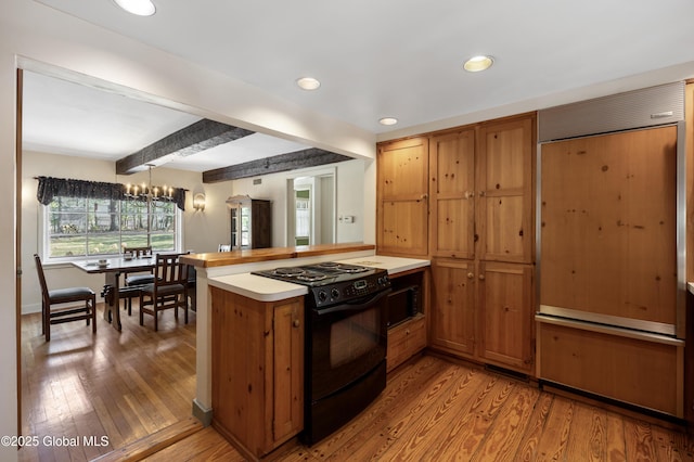 kitchen with brown cabinets, black range with electric stovetop, light wood-style flooring, a peninsula, and light countertops