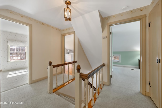 hallway with wallpapered walls, an upstairs landing, baseboards, and light carpet