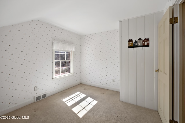 carpeted empty room with baseboards, visible vents, wallpapered walls, and lofted ceiling