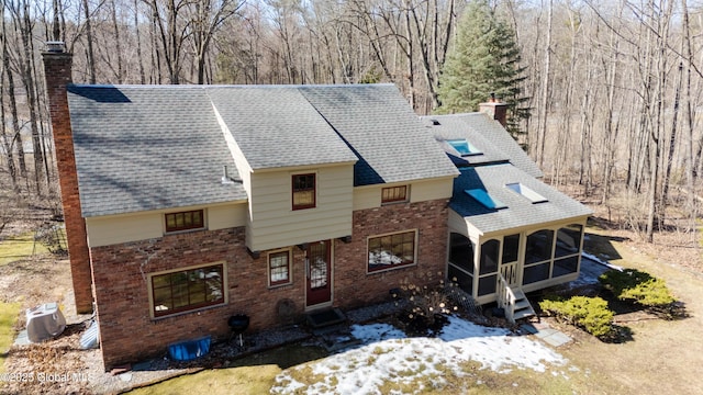 exterior space with a shingled roof, brick siding, a sunroom, and a chimney