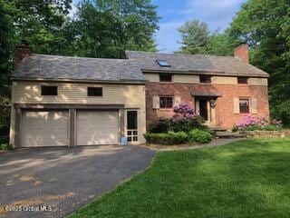 view of front facade featuring a front lawn, an attached garage, driveway, and a chimney