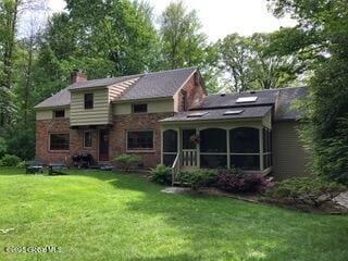 back of property with a lawn, a chimney, and a sunroom