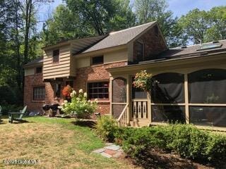 back of property with stone siding, a lawn, and a sunroom