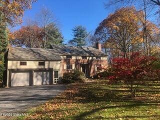 traditional-style house featuring aphalt driveway, a chimney, and a garage