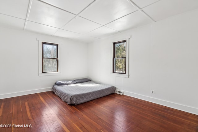 unfurnished bedroom with visible vents, a paneled ceiling, baseboards, and wood-type flooring