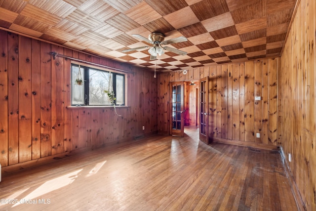 spare room featuring wooden walls, visible vents, ceiling fan, baseboards, and hardwood / wood-style floors